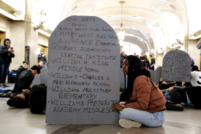 A young activist poses with the names of closed schools during a #NoCopAcademy protest at City Hall