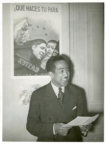Langston Hughes, American Poet, speaking and reciting poetry before the press and the United Nations "Comite De Coordination" in Paris, France after Spending 4 Months in Spain and Observing the Battle of Teruel, Spain (Communists Vs Government of Spain Aided by Germany). January 11, 1938; Typed on back: Americans, Observers of battle for Teruel lecture in Paris before returning to U.S.; Langston Hughes, American poet and John Davis, national secretary of the National American Negro Conference spoke for the first time on their return from Teruel at a meeting of the "Comite de /ciirdubatuib" in Paris. Hughes spent four months in Spain and Davis is sailing soon fo rthe U.S. to enlist Negro aid for the Spanish Government. The photo shows: Langston Hughes speaking at the meeting in Paris. Photo provided by The Archives at Queens Library.