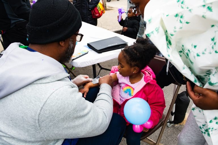 Young child holding balloon and getting a temporary tattoo at "Spend In The Black" street fest on 75th and King Dr. on April 19, 2025. Photo by Ash Lane for The TRiiBE®